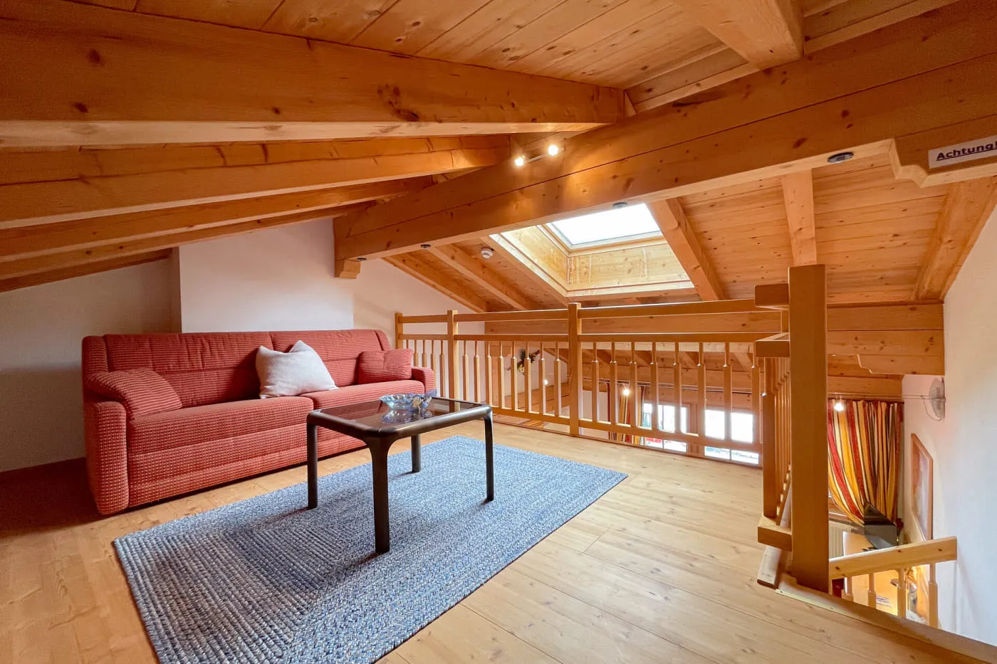 Großzügige Sitzecke auf der Holzgalerie der Suite Mountain mit Sofa, Tisch und Dachfenster